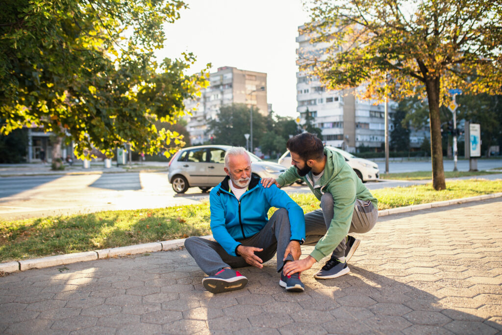 Son helping his father to stand up after his fall while jogging outdoors in city street.
